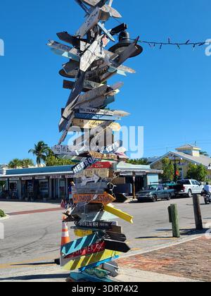 USAGE ÉDITORIAL SEULEMENT - KEY WEST FLORIDA : : Iconic Directional Signpost avec distances vers World Cities, Key West, Floride. Un haut panneau en bois rustique recouvert de flèches peintes à la main pointant vers diverses destinations mondiales, notamment « Wildwood Crest », « Berlin NH » et « Marblehead ». Le panneau est situé dans la zone portuaire historique sous un ciel bleu clair. Banque D'Images