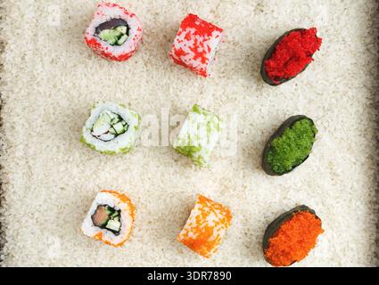 Rolls de Sushi colorés arrangés sur du riz blanc dans un plateau carré dans un cadre de restauration Banque D'Images