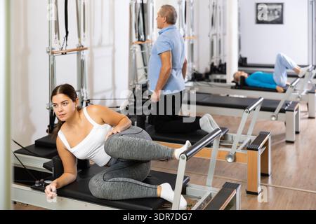 Jeune femme positive se concentrant sur l'exercice d'étirement sur le lit d'équipement de chaise Pilates en studio. Concept de mode de vie actif et sain Banque D'Images