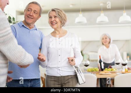 Deux couples de personnes âgées se accueillent chaleureusement alors qu'ils se réunissent pour un dîner festif de vacances à la maison Banque D'Images
