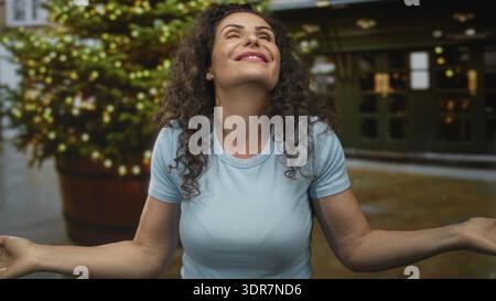 Jeune femme hispanique en chemise bleue souffle doucement baiser avec les deux mains sur la rue ensoleillée ; affection amour. Banque D'Images