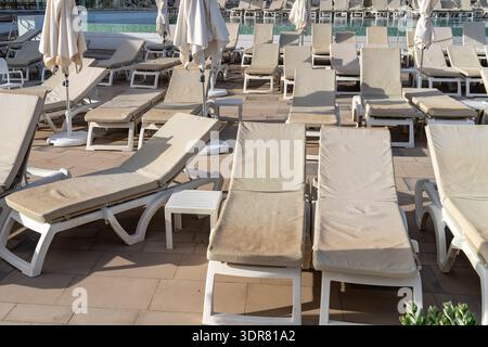 Une terrasse de piscine vide avec plusieurs chaises longues et parasols vous attend, invitant à la détente dans un environnement serein. Banque D'Images