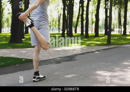 Coureur étire la jambe avant de courir dans un parc un jour ensoleillé Banque D'Images