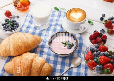 Le petit déjeuner composé de croissants, yaourts, café, fruits et miel est servi sur une nappe à carreaux Banque D'Images