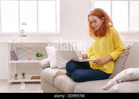 Jeune femme travaille sur ordinateur portable tout en étant assis sur canapé dans la salle lumineuse Banque D'Images