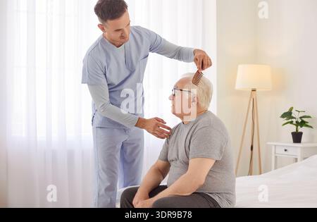 Aimable jeune soignant aidant homme âgé avec la routine du matin, se brossant les cheveux dans la maison de retraite. Banque D'Images