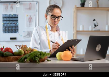 Conseillère en nutrition féminine faisant un plan de repas pendant le travail à la clinique de perte de poids. diététiste en blouse blanche écrivant prescription pour patient Banque D'Images