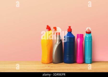 Collection de bouteilles de produits de nettoyage disposées sur une table en bois sur un fond rose Banque D'Images