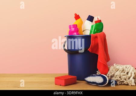 Fournitures et outils de nettoyage disposés dans un seau sur une table en bois sur un fond rose Banque D'Images