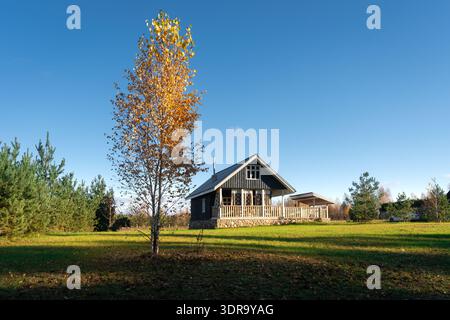 Une belle maison rurale avec une terrasse en bois confortable, entourée d'herbe verte luxuriante et d'une forêt sereine. Escapade idyllique parfaite à la campagne sur un c Banque D'Images