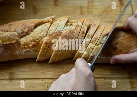 Gros plan d'une baguette soigneusement tranchée en morceaux minces sur une planche à découper en bois. La croûte croustillante et l'intérieur doux créent un contraste de texture riche. Banque D'Images