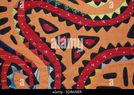 Panneau Guna mola du début du XXe siècle en coton. Rectangles de coton cousus ensemble, zones découpées et appliquées. Support en coton rouge imprimé avec des taches blanches. Le design appliqué en orange et rouge montre des formes en U bouclés avec des accents patchwork. Documentation technique textile, application des couleurs, méthodes appliquées, motifs géométriques et abstraits, et pratiques vestimentaires culturelles dans les vêtements indigènes d'Amérique centrale. Banque D'Images