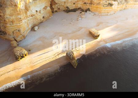 Vue aérienne des sables dorés rencontrant la mer turquoise sous les falaises imposantes, Praia da Marinha, District de Faro, Portugal. Banque D'Images