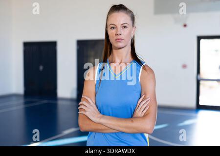 Dans le gymnase, joueuse de basket-ball debout avec les bras croisés, l'air confiant Banque D'Images