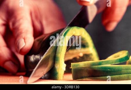 Couper le poivron vert sur une planche à découper. Homme coupant des poivrons dans la cuisine. Trancher les légumes Banque D'Images