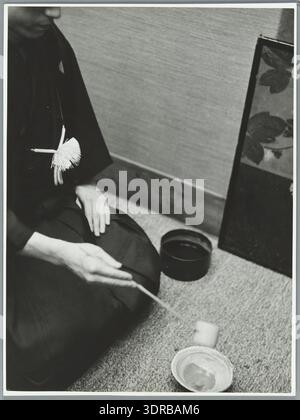 La photographie montre une cérémonie du thé japonaise en 1938 en se concentrant sur la posture particulière des mains lorsque l'on verse de l'eau chaude. L'image illustre la technique cérémonielle, l'étiquette, la pratique culturelle japonaise, l'utilisation des ustensiles, le processus formel, méthode d'enseignement, communication visuelle et coutumes sociales historiques. Il documente les positions traditionnelles des mains japonaises et les actions ritualisées pendant la préparation du thé. Banque D'Images