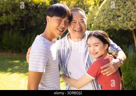 Père souriant et fils et fille adolescents embrassant à l'extérieur, profitant du temps ensemble dans le jardin Banque D'Images