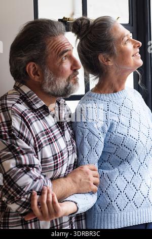 Couple mature regardant par la fenêtre, profitant d'un moment paisible à la maison ensemble Banque D'Images