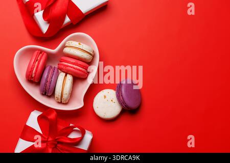 Macarons colorés élégamment disposés dans un bol en forme de cœur, accompagnés d'un charmant coffret cadeau Saint-Valentin Banque D'Images