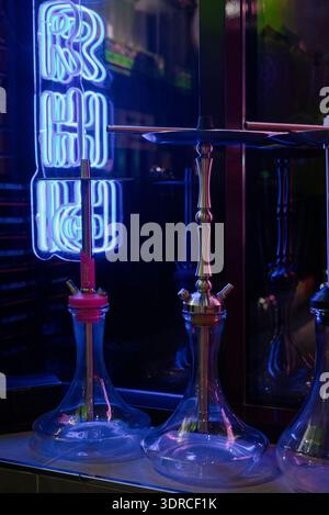 Hookahs en verre sur un comptoir de bar dans une discothèque avec éclairage au néon.hookahs modernes en verre et en métal dans un salon de hookah avec néon bleu Banque D'Images