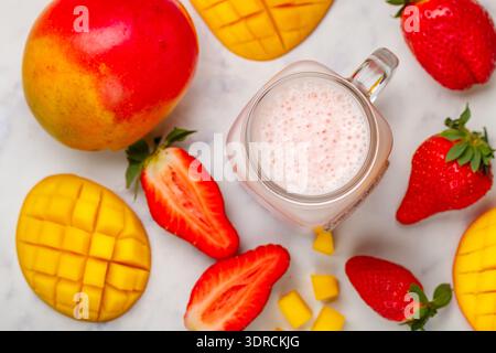Smoothie ou milkshake à base de fraises fraîches, mangue, yaourt ou lait et glaçons dans un pot Mason sur une table en marbre. Concept Banque D'Images