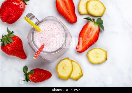 Smoothie ou cocktail milkshake à base de fraises fraîches, banane, yaourt ou lait et glaçons dans un pot Mason sur une table en marbre Banque D'Images