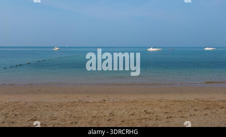 Bateaux amarrés dans les eaux peu profondes d'une mer calme par un beau matin vu d'une plage de sable, reflétant la vie côtière paisible. Idéal pour les voyages Banque D'Images