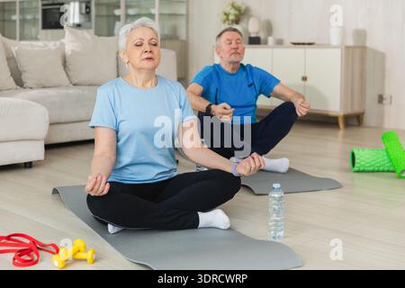 Méditation de pleine conscience de yoga. Couple adulte senior pratiquant le yoga à la maison. Femme de vieux mari d'âge moyen assise dans la posture du lotus Banque D'Images