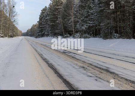 une route pavée couverte de glace pour les voitures à travers une forêt d'hiver dans la neige , une voie étroite couverte de neige des voitures dans la forêt en hiver se Banque D'Images