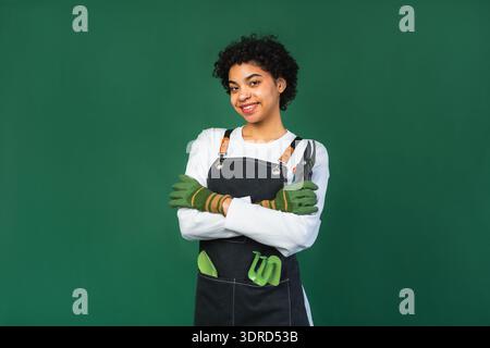 Gestion de sa propre entreprise. Femme africaine fleuriste avec sécateur portant tablier isolé sur fond vert. Heureux petit business owne Banque D'Images