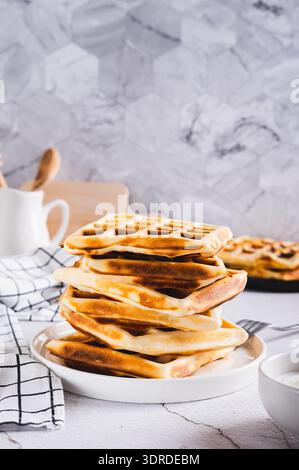 Pile de gaufres belges fraîchement cuites sur l'assiette et crème sure dans le bol sur la table vue verticale Banque D'Images