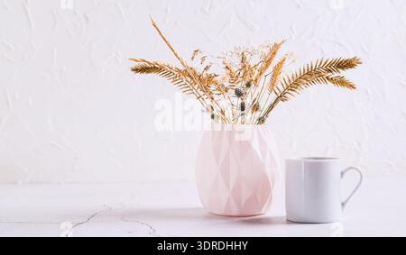 Vase figuré avec des fleurs séchées et une tasse de café sur fond blanc Banque D'Images