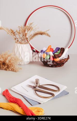 Toile, fil de broderie, ciseaux, aiguille, dé et cerceau de point de croix sur la vue verticale de la table Banque D'Images