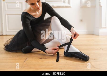 Ballerine met des chaussures pointe sur la jambe en classe de danse. Danseuse de ballet classique femme dans un studio de danse. Ballerine mettant sur la noue Banque D'Images