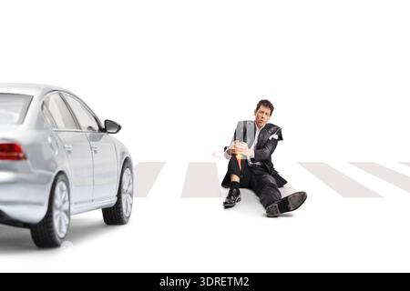 Homme blessé dans un costume déchiré assis sur un passage pour piétons après avoir été heurté par une voiture Banque D'Images