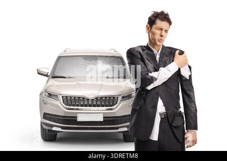 Homme avec bras blessi dans un costume déchiré debout devant une voiture avec un pare-brise cassé isolé sur fond blanc Banque D'Images