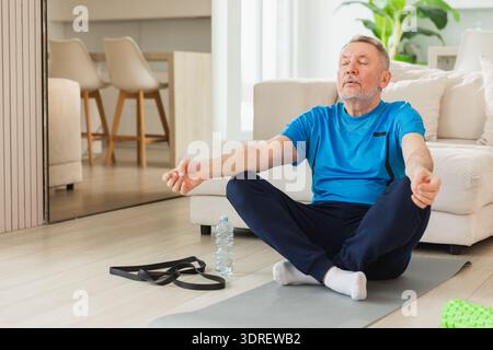 Méditation de pleine conscience de yoga. Homme adulte senior pratiquant le yoga à la maison. Grand-père âgé de mi-âge assis dans le lotus pose sur y Banque D'Images