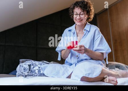 Femme blanche souriante âge moyen 40s prenant des médicaments à la maison sur le lit Banque D'Images