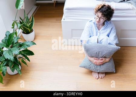 Femme blanche pensive dans ses années 40 assise sur le sol serrant l'oreiller Banque D'Images