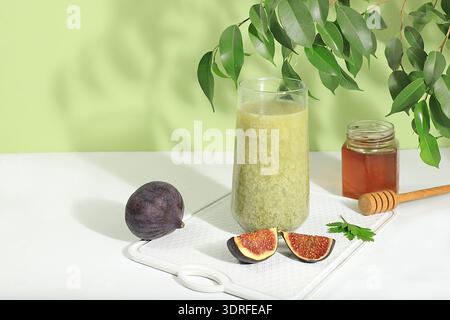 Latte au thé vert Matcha dans un verre avec des figues et du miel sur un fond clair moderne avec des feuilles tropicales. Nature morte moderne sur un Banque D'Images