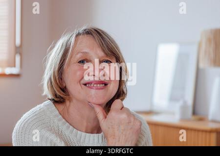 Portrait rapproché d'une femme âgée en pull. Une belle dame d'âge moyen en vêtements décontractés sourit dans le salon Banque D'Images