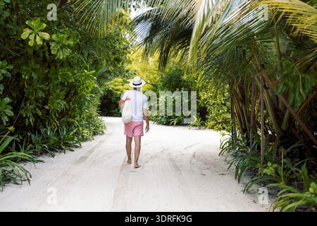 Un jeune homme dans un T-shirt blanc et un chapeau sur un fond de plantes tropicales vertes Banque D'Images