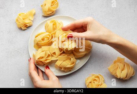 Femme chef organisant des nids de pâtes crues sur une assiette blanche Banque D'Images