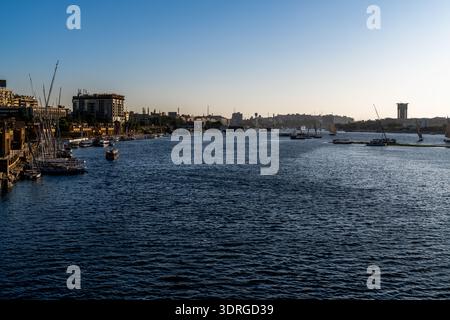 Vue large sur le fleuve Nil à Assouan, en Égypte, avec des bateaux amarrés le long du front de mer urbain montrant la vie quotidienne de la ville de trafic fluvial et les vagues étendues Banque D'Images