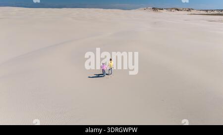 Couple marchant main dans la main sur une plage de sable sereine au Danemark sous un ciel bleu vif Banque D'Images