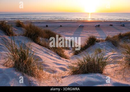 Coucher de soleil sur la plage sereine au Danemark présentant des dunes et des véhicules à l'heure dorée Banque D'Images