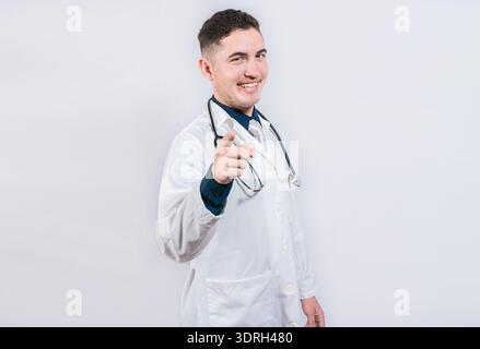Beau docteur pointant la caméra. Médecin amical et souriant pointant vers vous, jeune médecin pointant vers vous Banque D'Images