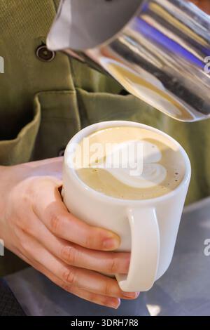Le barista confectionne un cappuccino avec du latte en forme de cœur Banque D'Images
