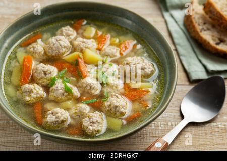 Soupe aux boulettes de viande avec des légumes dans un bol vert, fond en bois Banque D'Images