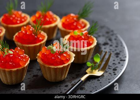 Délicieux caviar rouge de saumon sur plaque noire, fond noir Banque D'Images